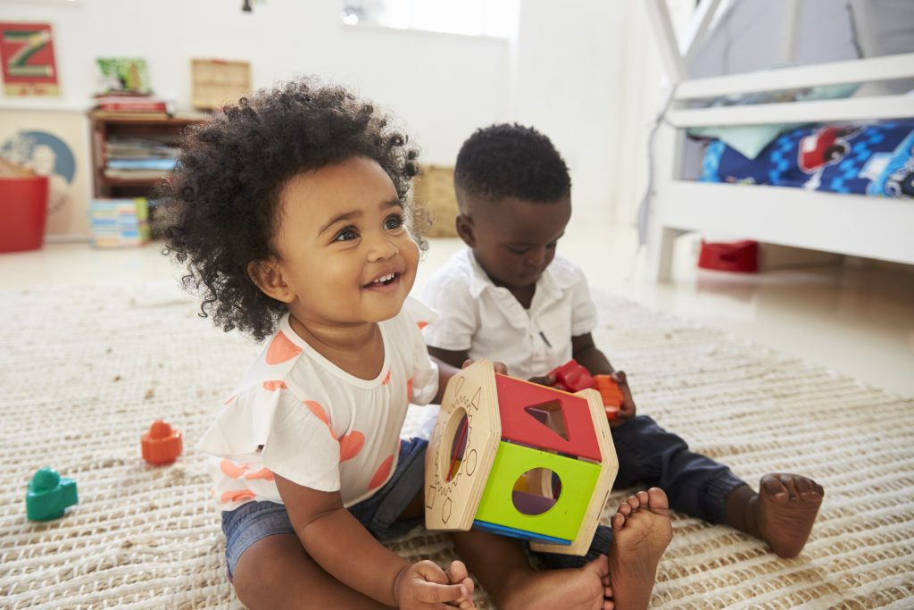 Baby Boy And Girl Playing With Toys In Playroom Together